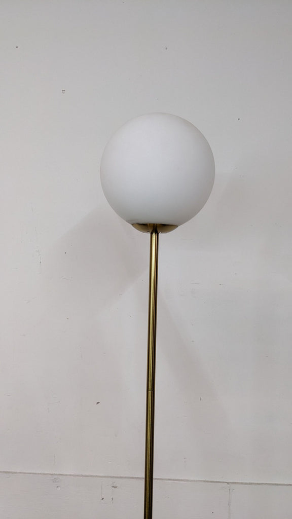 Close-up of Reperch brass floor lamp, highlighting the white spherical shade against a plain wall.