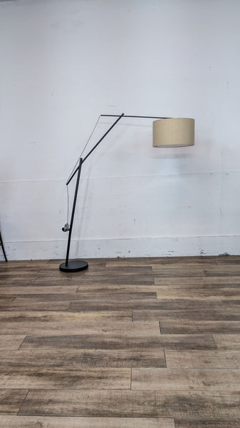 Reperch floor lamp with a long, angled arm and beige drum shade in a minimalist setting.