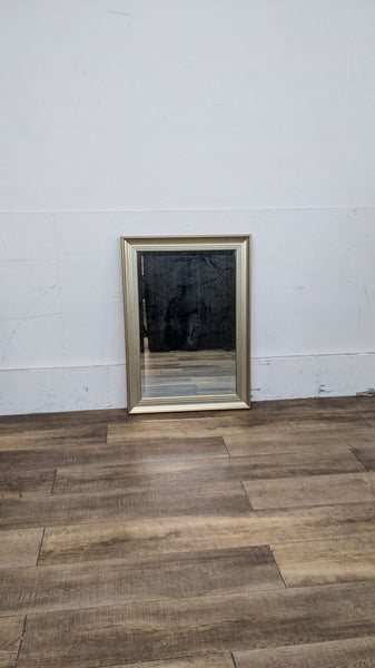 Gold-framed beveled wall mirror by Reperch on wooden floor.