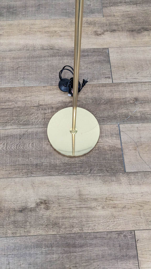 Gold base of a Reperch floor lamp on wooden flooring.