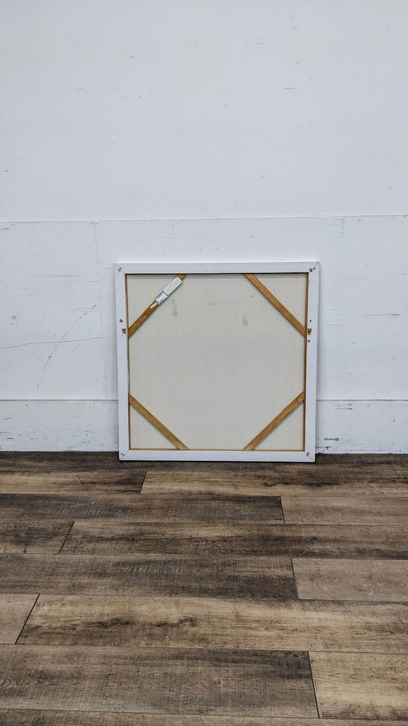 Back of a framed square canvas with wooden supports visible.