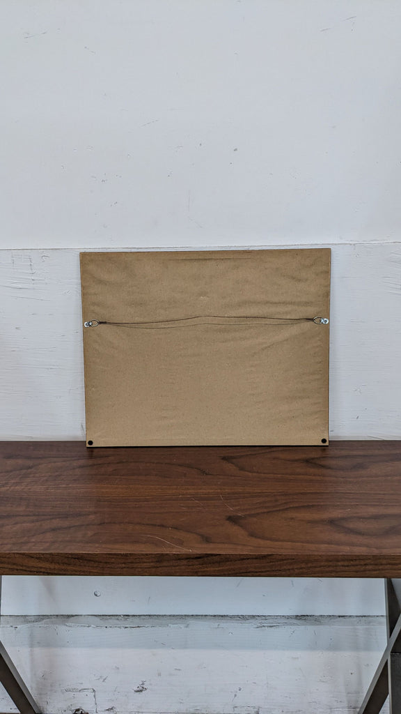 Rear view of a framed print with a hanging wire on a wooden shelf.