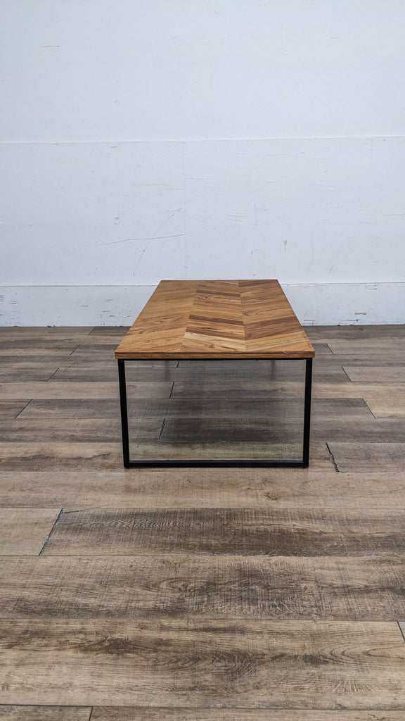 Square-shaped Reperch coffee table featuring a wood top with chevron design and thin metal frame, on a wood-patterned floor.