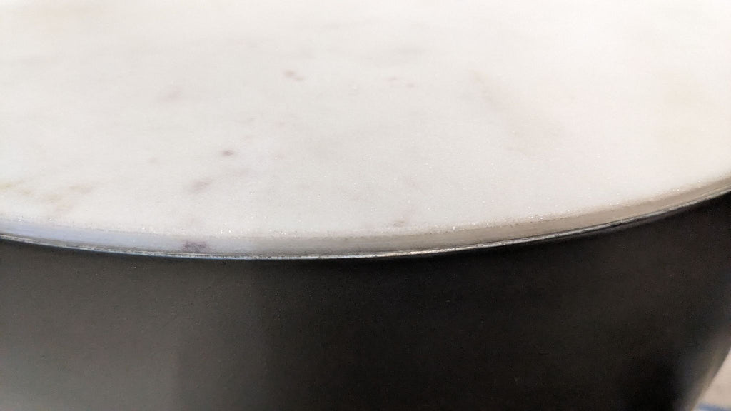 3. Close-up of the edge of a CB2 marble-topped side table with a sleek, dark base.