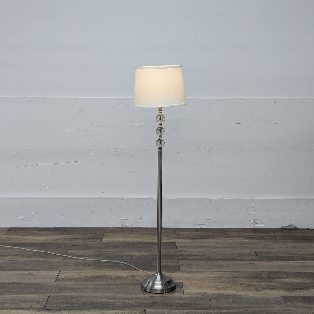 Reperch lamp lit with a white shade, standing in an empty room.