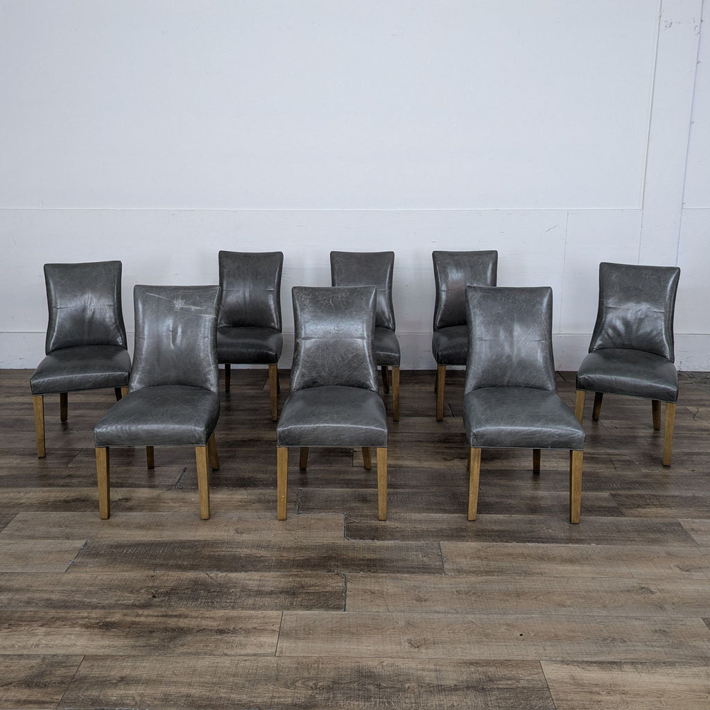 Set of eight gray leather dining chairs with wooden legs on wood flooring.