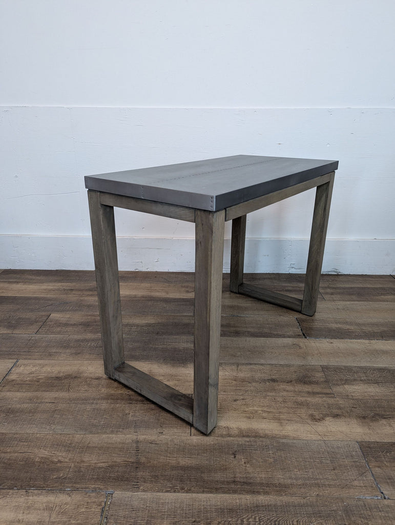 Single gray-topped bench with wooden legs on a wooden floor.