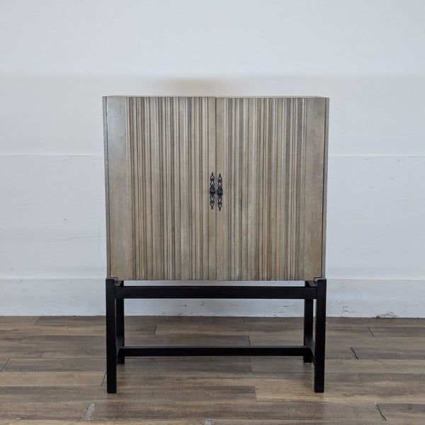 1. Reperch cabinet with ribbed wood doors and ornate handles on a black metal frame, closed view.