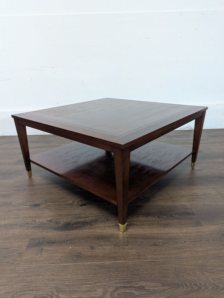 Square Reperch coffee table with a polished finish, sturdy legs, a lower shelf, and gold accents on the feet.