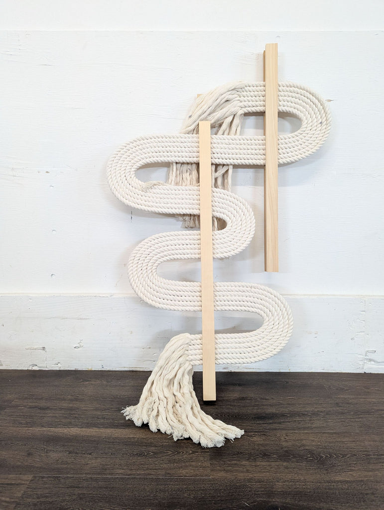 3. Vertical fiber art by West Elm Candice Luter, with white coiled rope, wooden slats, and long loose tassels at each end.