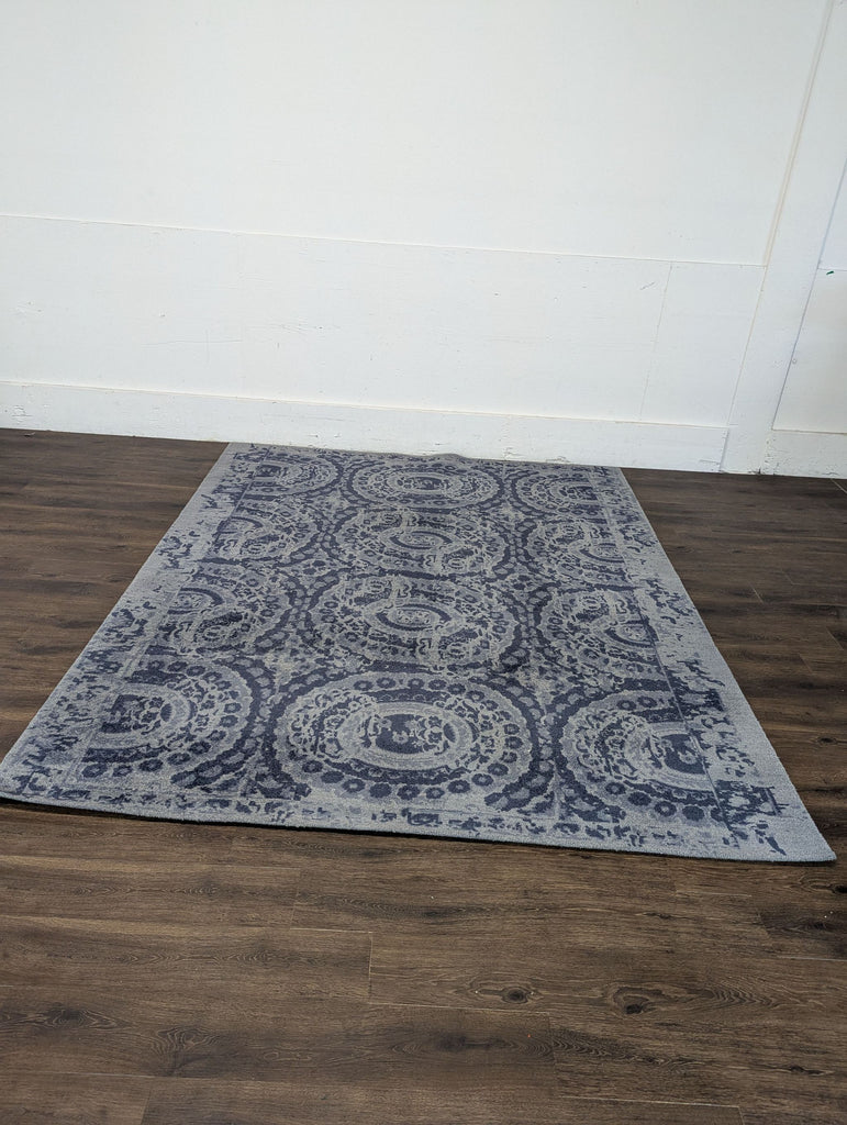 2. Blue and grey patterned Crate and Barrel rug displayed on a wooden floor against a plain white wall.  