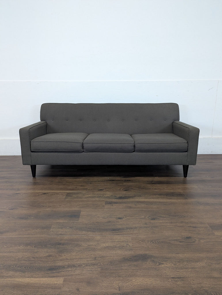 Reperch 3-seat gray sofa with tufted backrest shown on wood floor, photographed head-on against a white wall.  