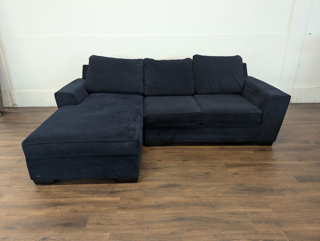 3. Navy blue sectional from 2 year old couch brand, displayed in a minimalist room with plain white walls.