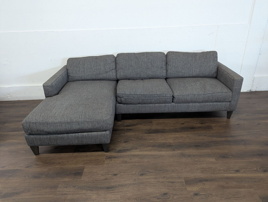 3. Gray fabric Room and Board sectional, left-facing chaise, displayed in an empty room with wood flooring.