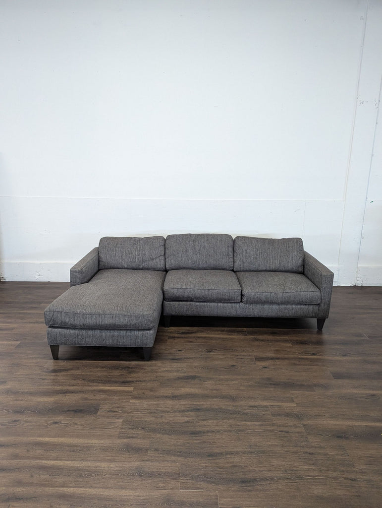 2. Room and Board gray sectional sofa with left chaise on a dark wood floor, against a plain white wall.