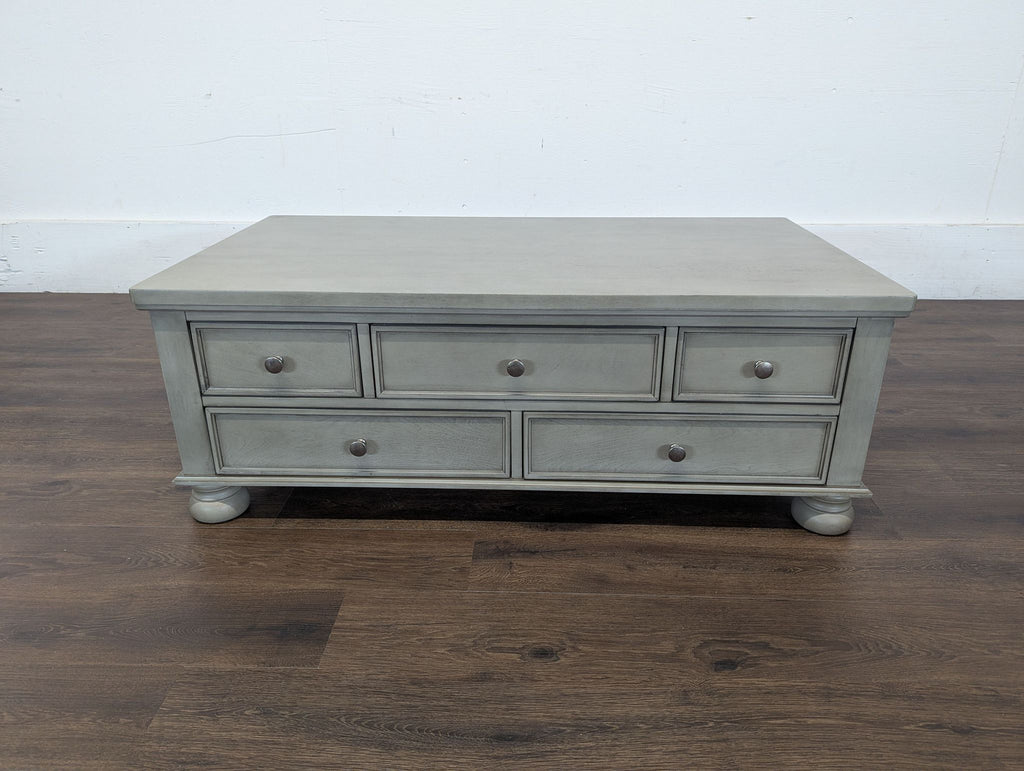 3. Front view of a Reperch coffee table in gray with five drawers and rounded feet, standing on a hardwood floor.