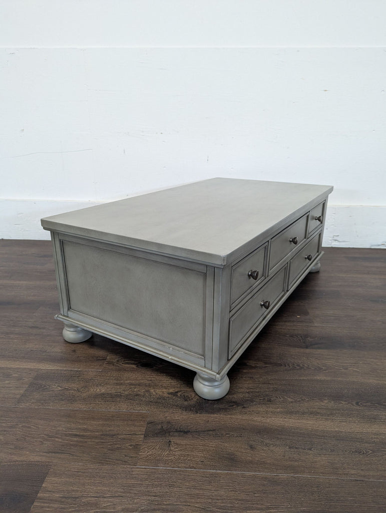 2. Gray Reperch coffee table featuring six drawers and decorative round feet, displayed on wood flooring.