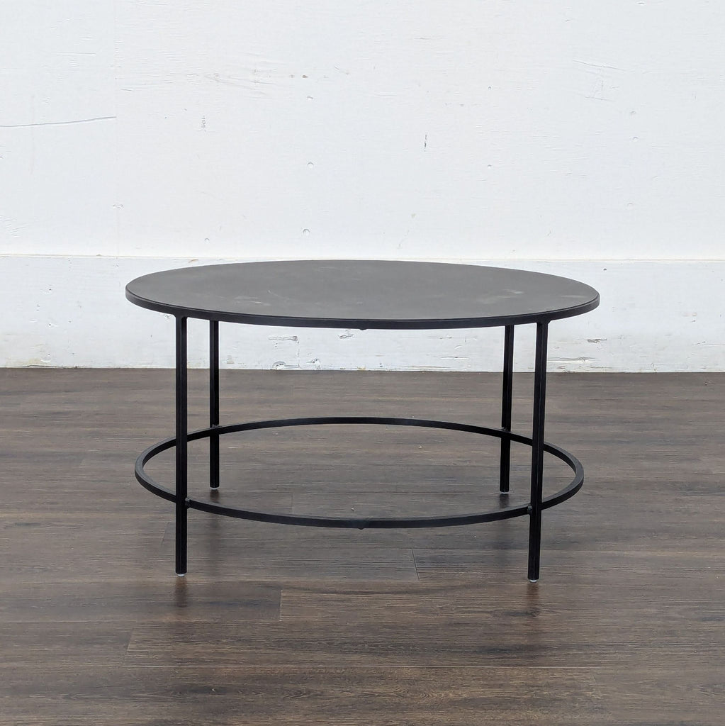 2. Minimalist round coffee table by Reperch with metal legs and black top, placed on a wood floor.