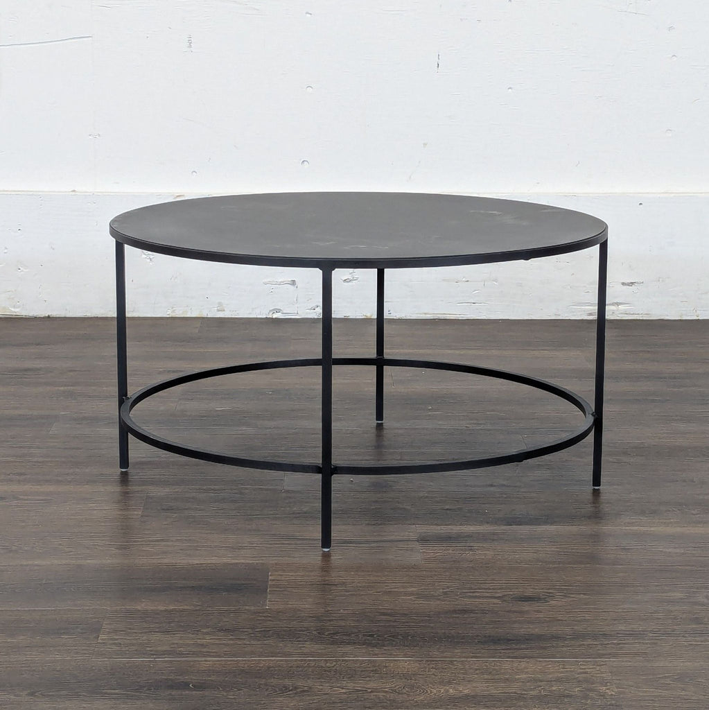 3. Reperch round black metal coffee table, featuring a contemporary open-frame design against a white wall.