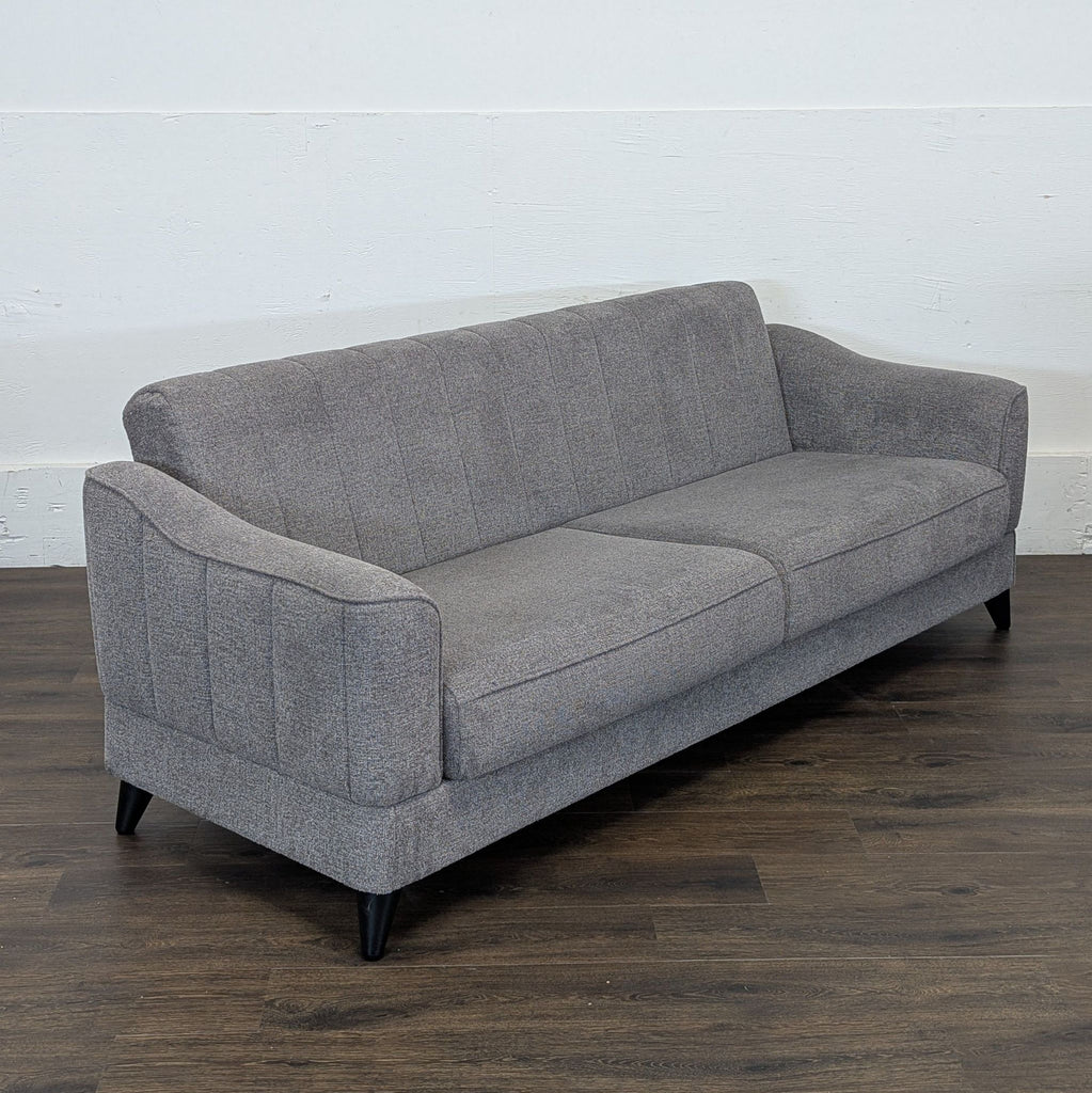 3. Angled view of a gray 3-seat sofa with armrests and slender black legs, on a wood floor in a minimal room.
