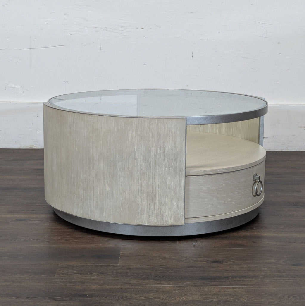 3. Side view of a circular coffee table featuring a glass top, open shelf, and sleek wood paneling with a drawer.
