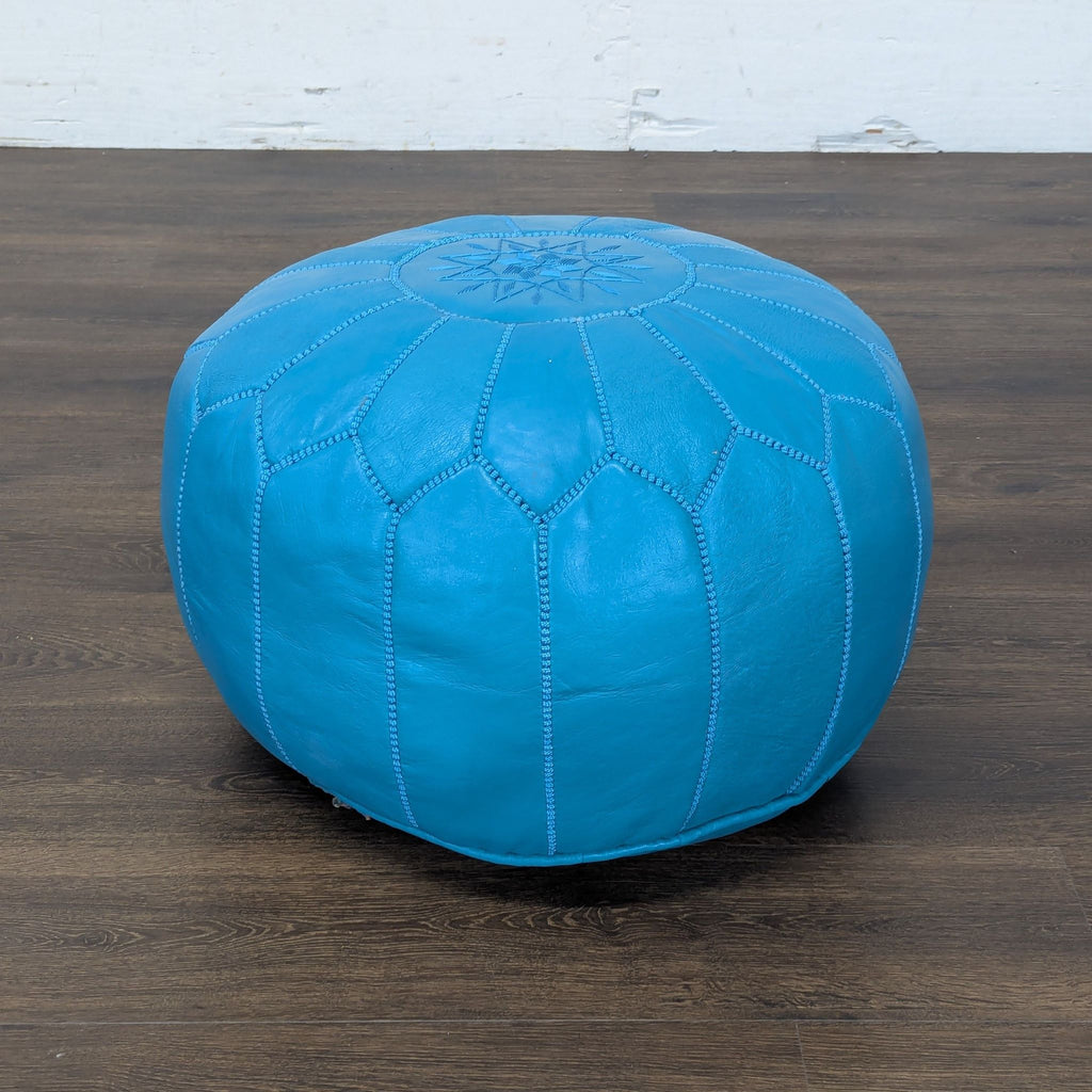 1. Round blue leather ottoman from Reperch with decorative stitching, shown on a dark wood floor.