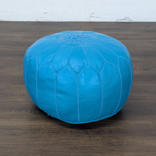 1. Round blue leather ottoman from Reperch with decorative stitching, shown on a dark wood floor.