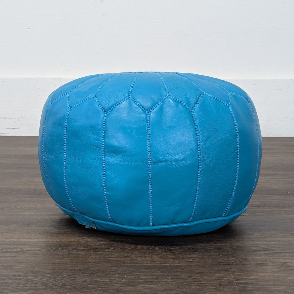 3. Side view of a Reperch blue leather ottoman with stitched panels, placed against a white wall.