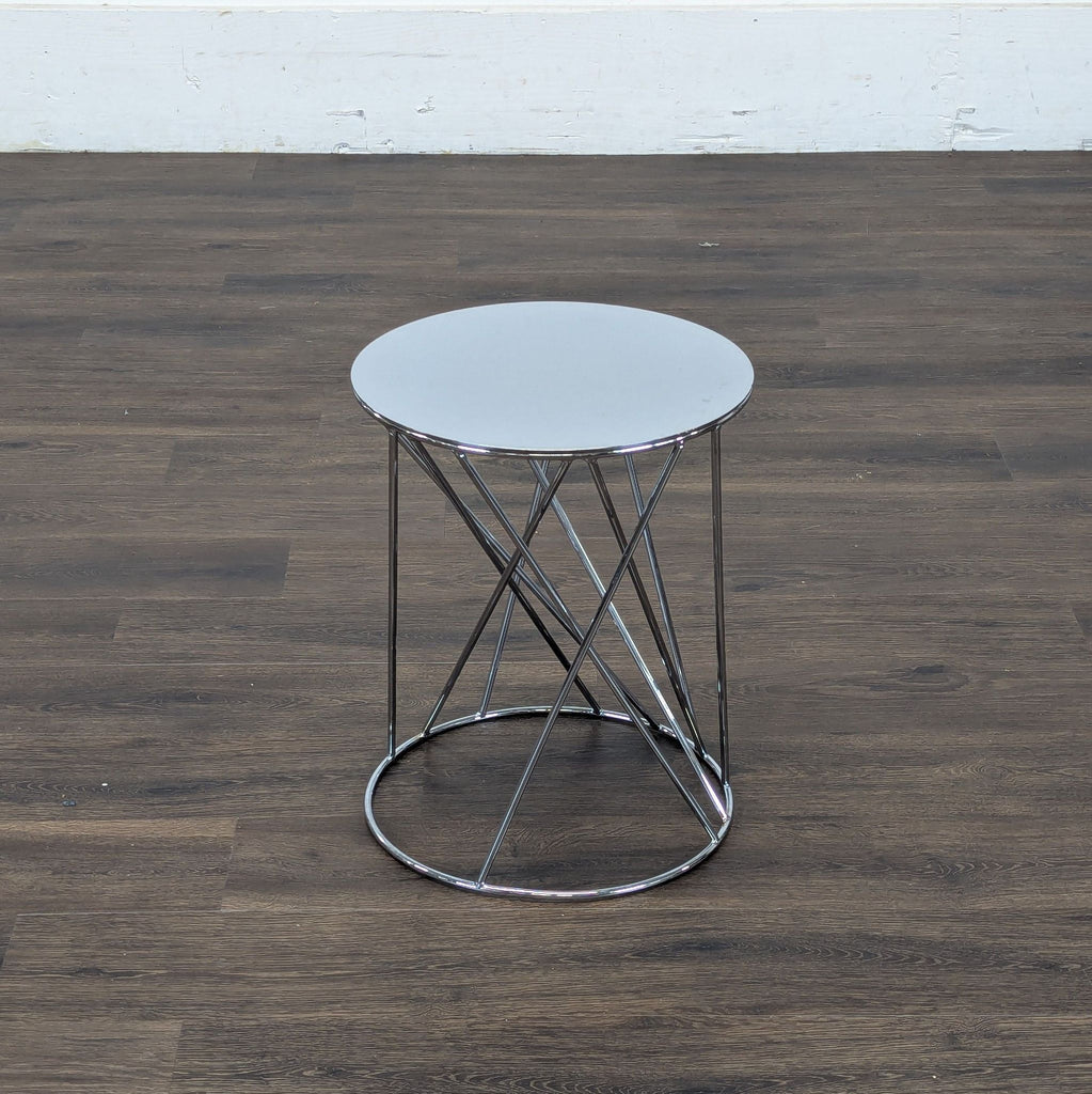 3. Contemporary Reperch end table, round glass top and intersecting chrome legs, set against wood flooring.