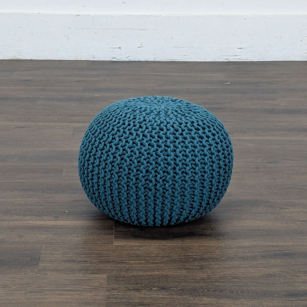 1. Blue knitted pouf ottoman from Reperch, round and textured, on a dark wooden floor.