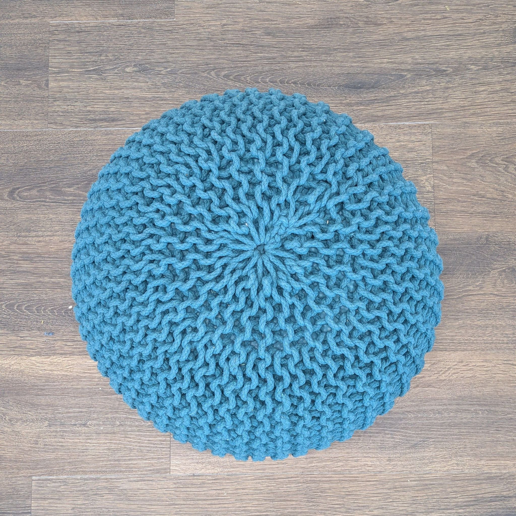 3. Top-down view of a round blue Reperch pouf ottoman with detailed knit pattern, on wood flooring.
