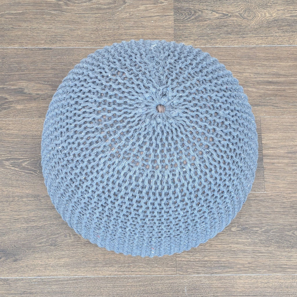 3. Top view of a gray crocheted Reperch ottoman, showcasing its detailed woven pattern on wooden flooring.
