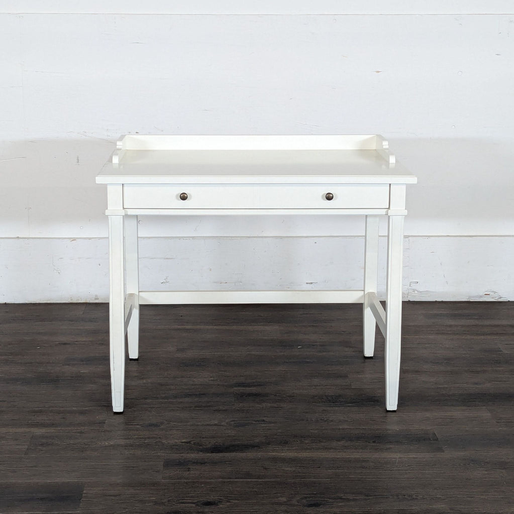 1. White Reperch writing desk with single drawer and raised back edges, seen against a wood floor and white wall.