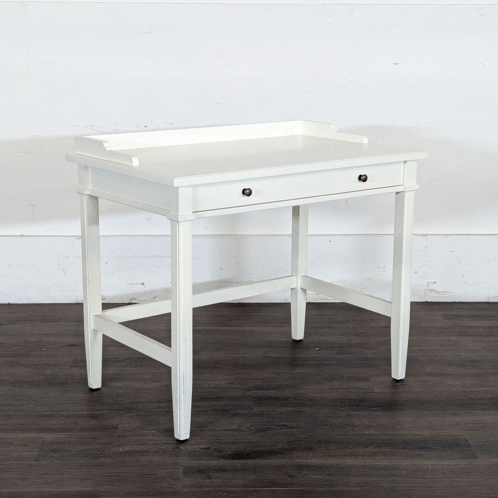 2. Angled view of a Reperch white desk with classic tapered legs and a central drawer, in a minimal setting.