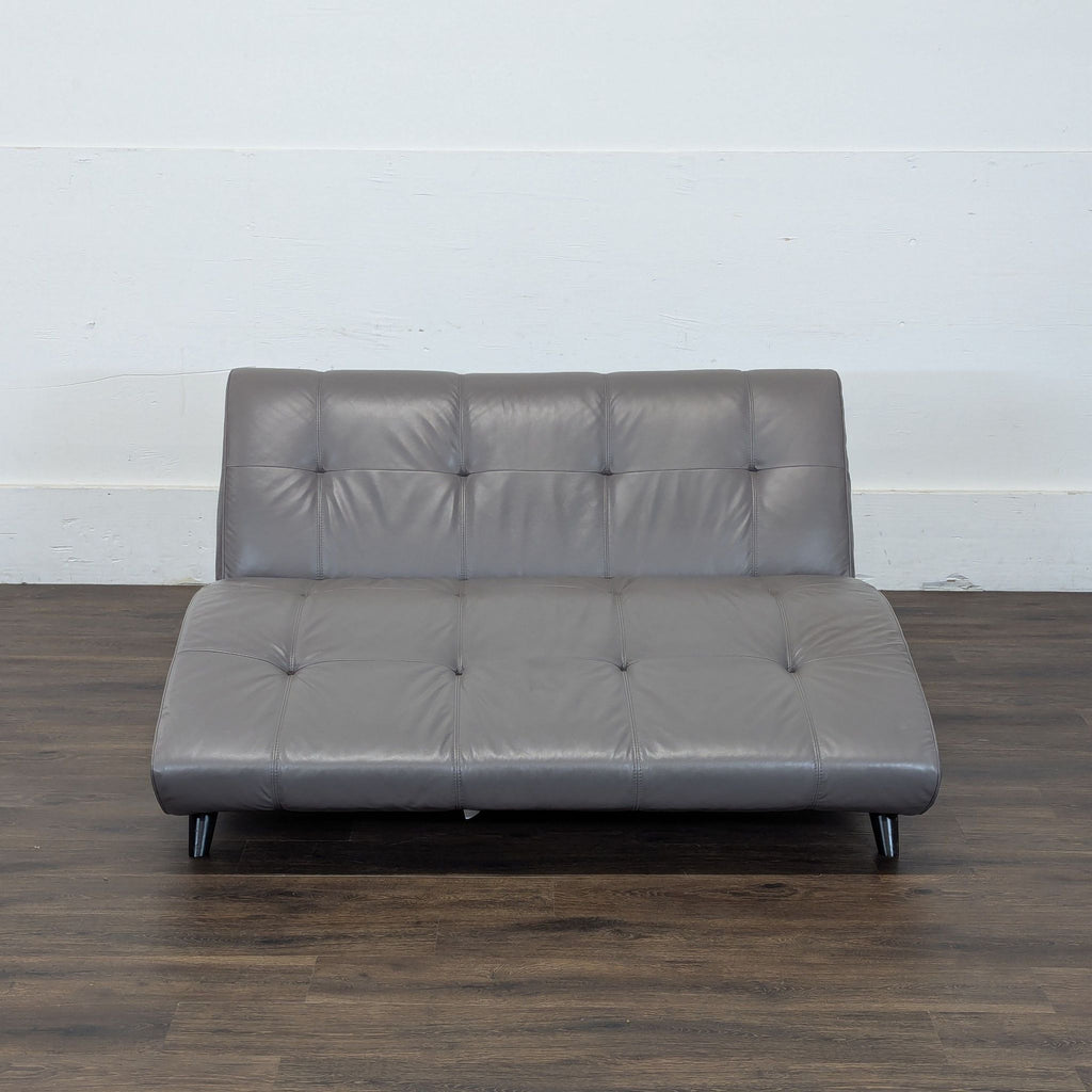 2. EQ3 brand gray faux leather futon with tufted detail, shown against a white wall and wooden floor.  