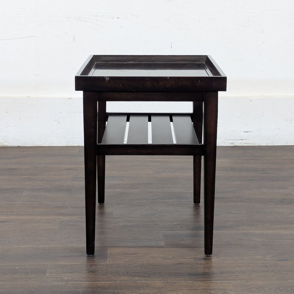 3. Reperch side table in dark wood, viewed from the side, highlighting the tray-like top and slatted shelf.