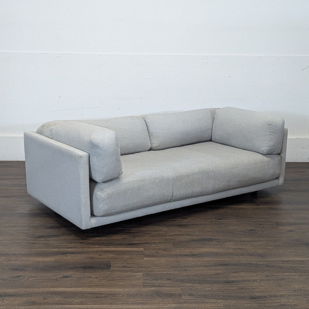 Modern BluDot 3-seat sofa in light gray upholstery, angled view highlighting its boxy armrests and deep seat.