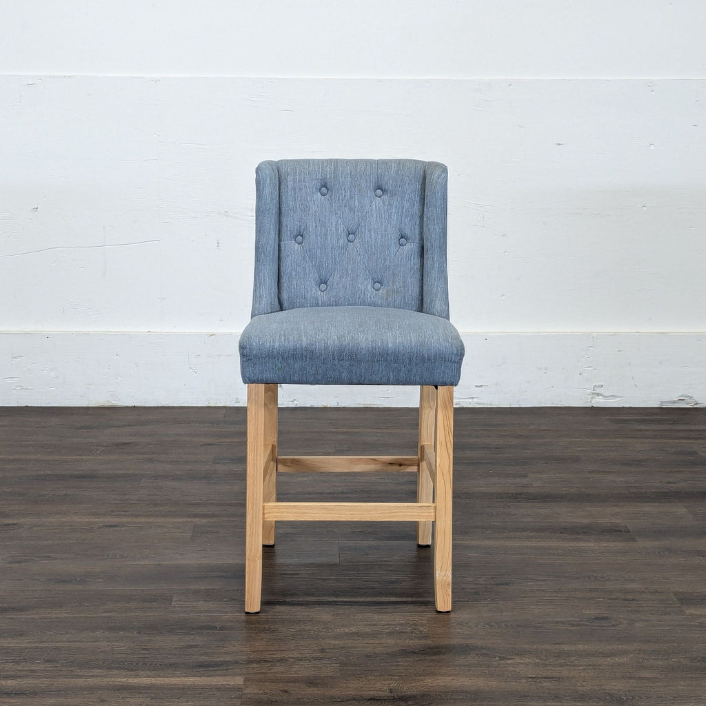 1. Reperch stool with blue tufted fabric backrest and seat, and light wooden legs, shown from the front.