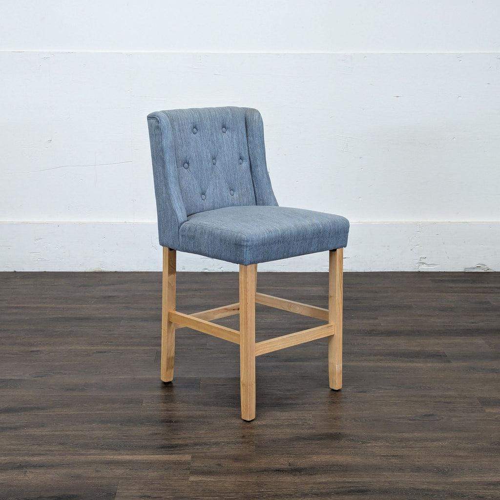 2. Reperch blue upholstered stool with button-tufted backrest and natural wood base, angled side view.