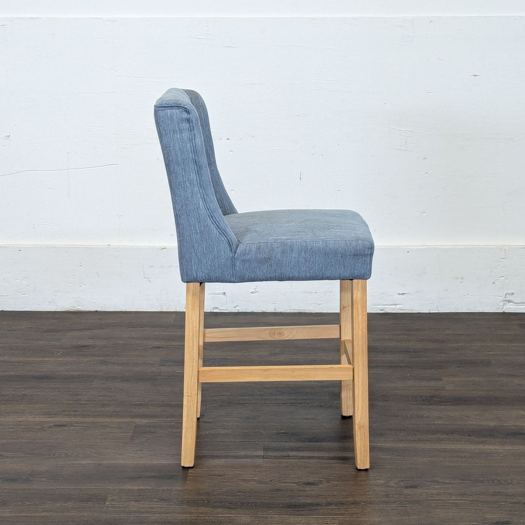 3. Side view of a Reperch stool displaying blue fabric upholstery and light wood legs on a dark floor.