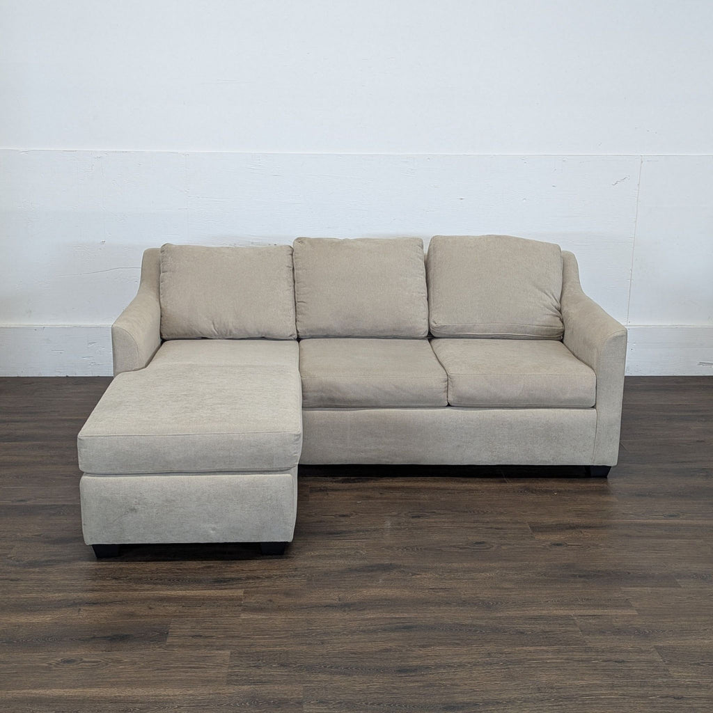 3. Couch brand 3-seat beige sectional sofa with chaise, displayed against a plain wall on a dark wood floor.