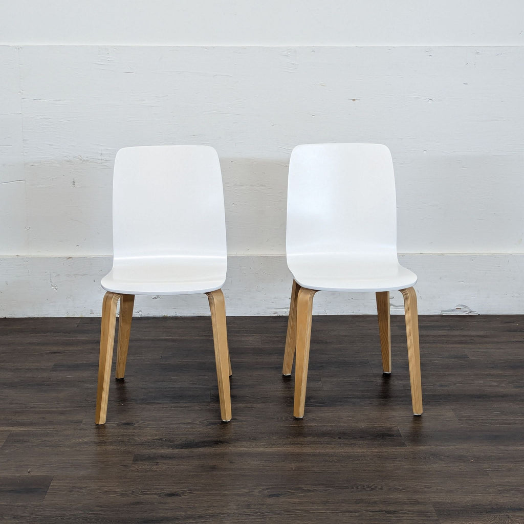 Pair of Reperch white dining chairs with wooden legs, placed side by side against a plain wall.