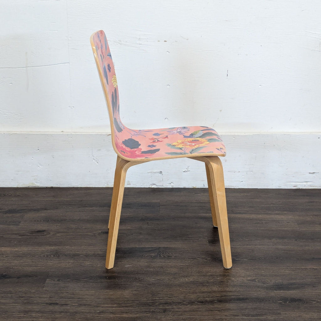 3. Profile shot of a Reperch dining chair showing curved pink floral seat and light wooden legs, on a dark floor.