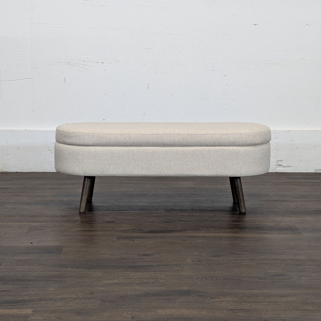 3. Minimalist light beige Walmart Sofa bench with dark wooden legs, displayed against a plain white wall on dark flooring.