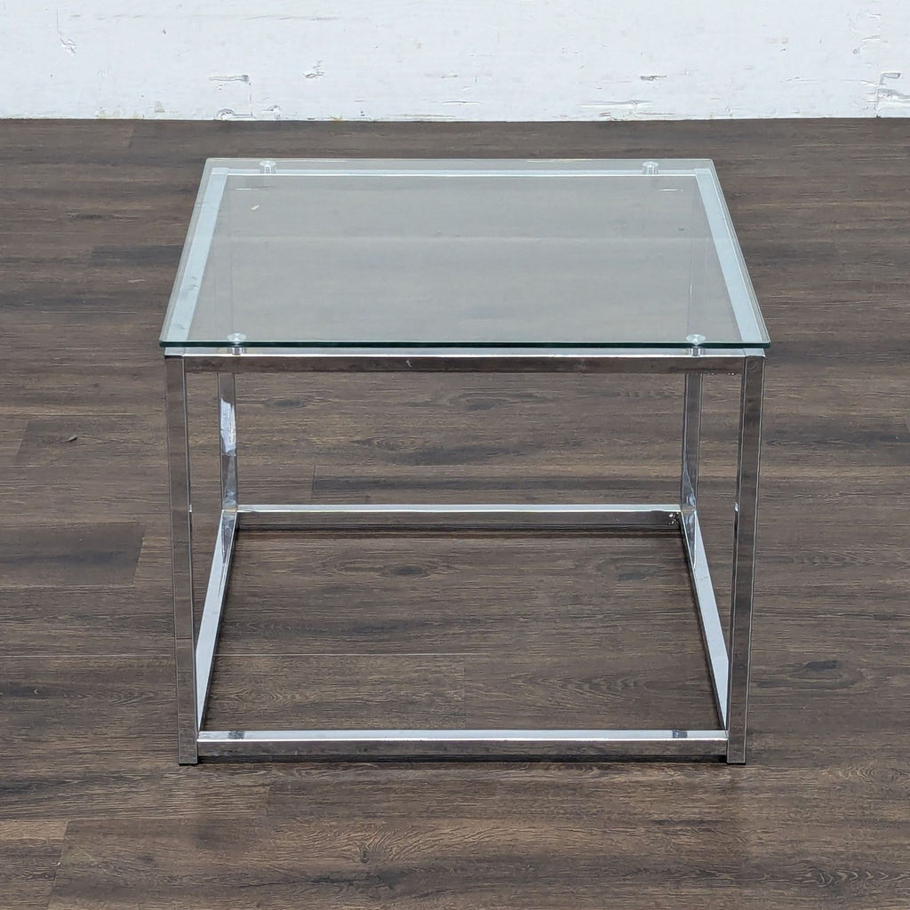 2. Modern end table featuring a clear glass top and chrome square legs on a dark wood floor.