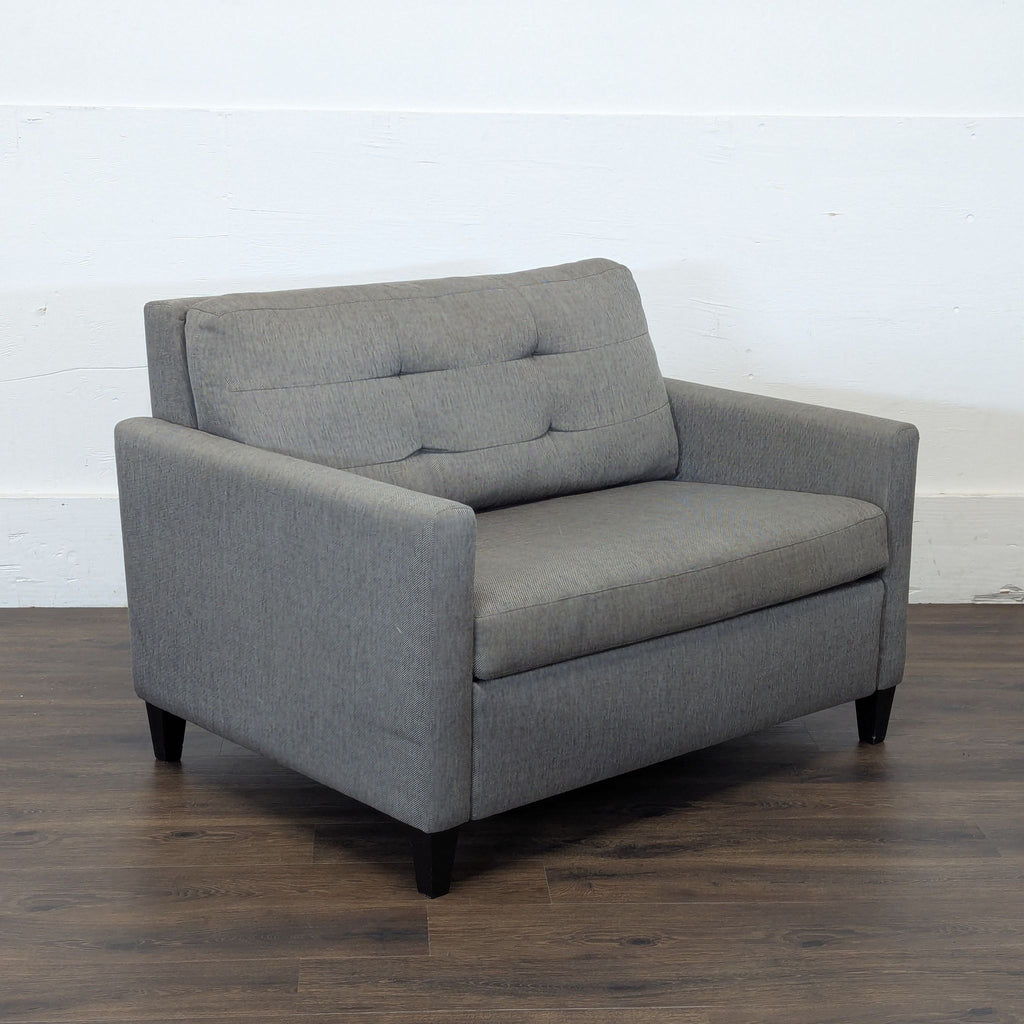 3. Angled view of a Crate & Barrel gray sleeper sofa, showing tufted backrest and slim armrests on wood flooring.