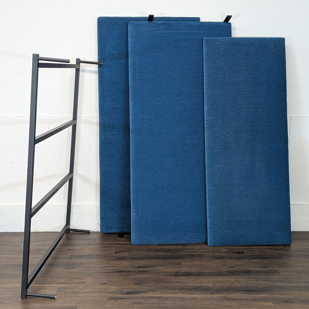 2. Disassembled Room & Board blue bed frame parts and black metal support against a wall indoors.