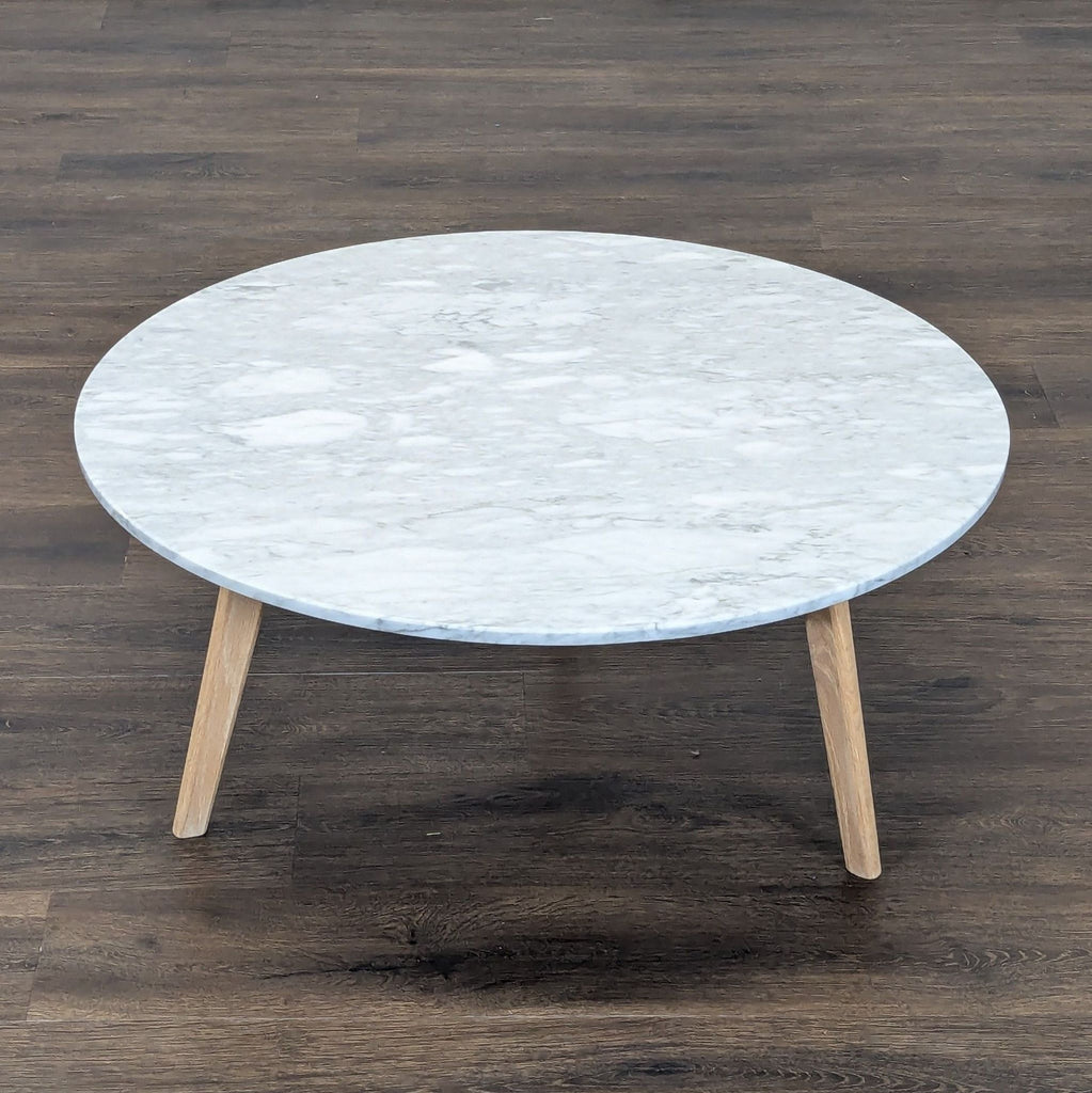 2. Article brand coffee table with white marble top and three natural wood legs on wooden floor.