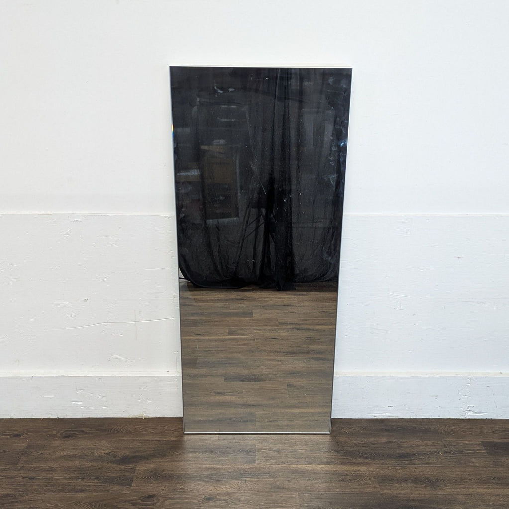 2. Minimalist Reperch mirror with sharp edges standing upright on a wood floor, reflecting a dark curtain.