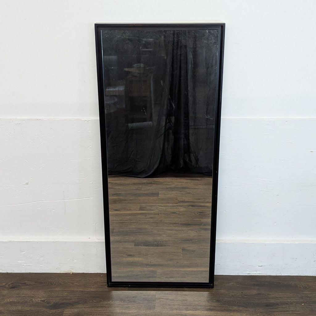 3. West Elm wall mirror with black frame standing against a white wall and wooden floor, empty background.